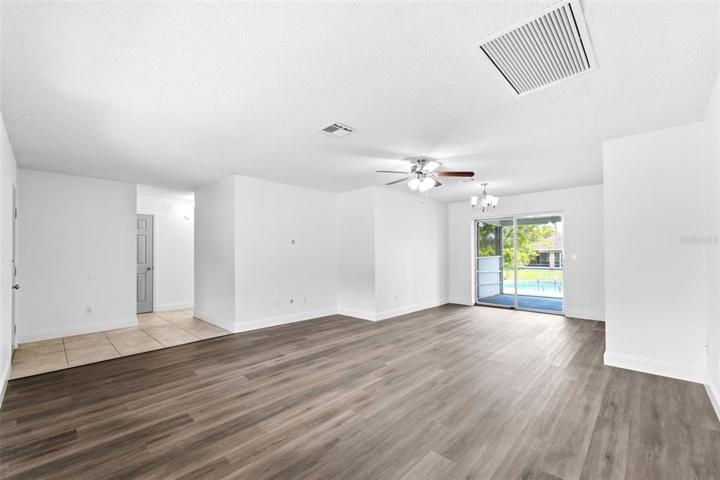 A spacious living room features wood-look flooring, white walls, a ceiling fan, and sliding glass doors — 1360 N OLD MILL DRIVE, DELTONA, FL