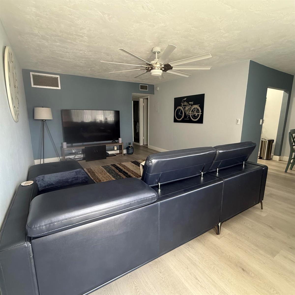 A living room features a dark blue sectional sofa, a television, and a ceiling fan — 2102 Lake Osborne Drive # 20, FL 33461, FL