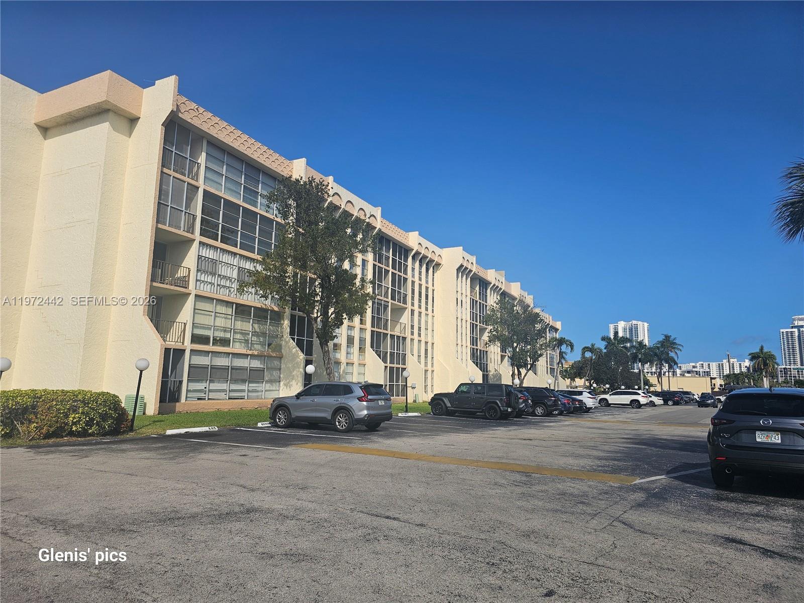 A multi-story apartment building with a parking lot in the foreground under a clear sky — 801 Three Islands Blvd # 218, Hallandale Beach FL 33009, HALLANDALE BEACH, FL