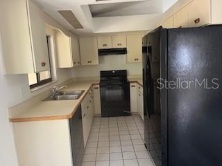 A kitchen features light-colored cabinets, black appliances, a double sink, and white tile flooring — 59 WELLWOOD LANE UNIT A & B, PALM COAST, FL