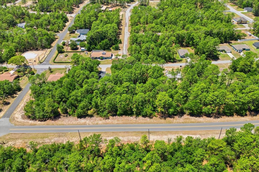 An aerial view shows a wooded lot bordered by a road and nearby residential houses — 10858 N ELKCAM BOULEVARD, CITRUS SPRINGS, FL