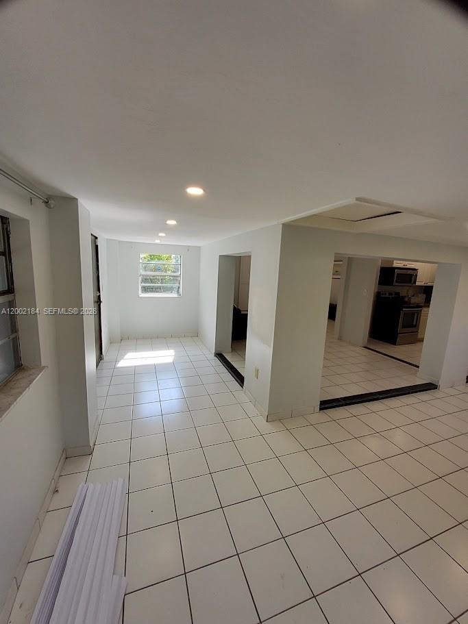 A bright room with white tile floors leads to a kitchen area with appliances — 1348 NE 176th St, North Miami Beach FL 33162, NORTH MIAMI BEACH, FL