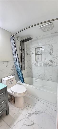 A bathroom features a white toilet, a bathtub with a shower panel, and marble-patterned tile — 911 WASHINGTON AVENUE SW UNIT 118, LARGO, FL
