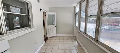 A sunroom with tiled flooring, large windows, and a white door leading to the interior — 911 WASHINGTON AVENUE SW UNIT 118, LARGO, FL