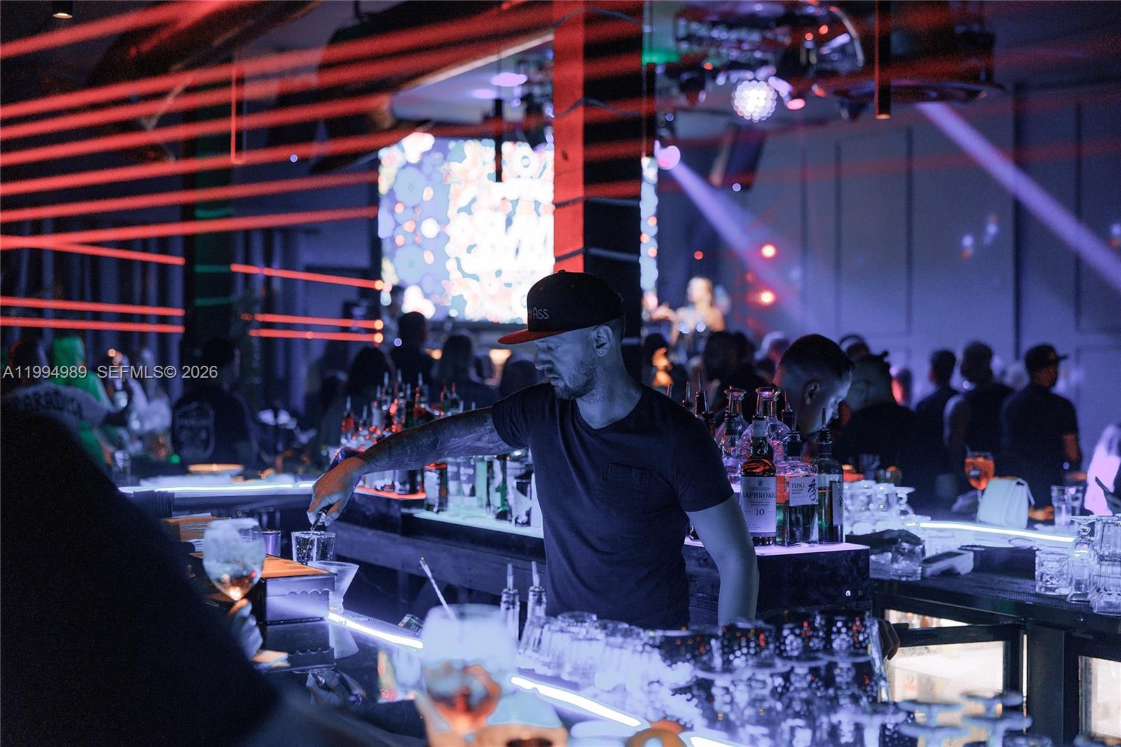 A bartender works behind a lit bar in a dimly lit, modern nightclub setting — 115 S 20th Ave, Hollywood FL 33020, HOLLYWOOD, FL