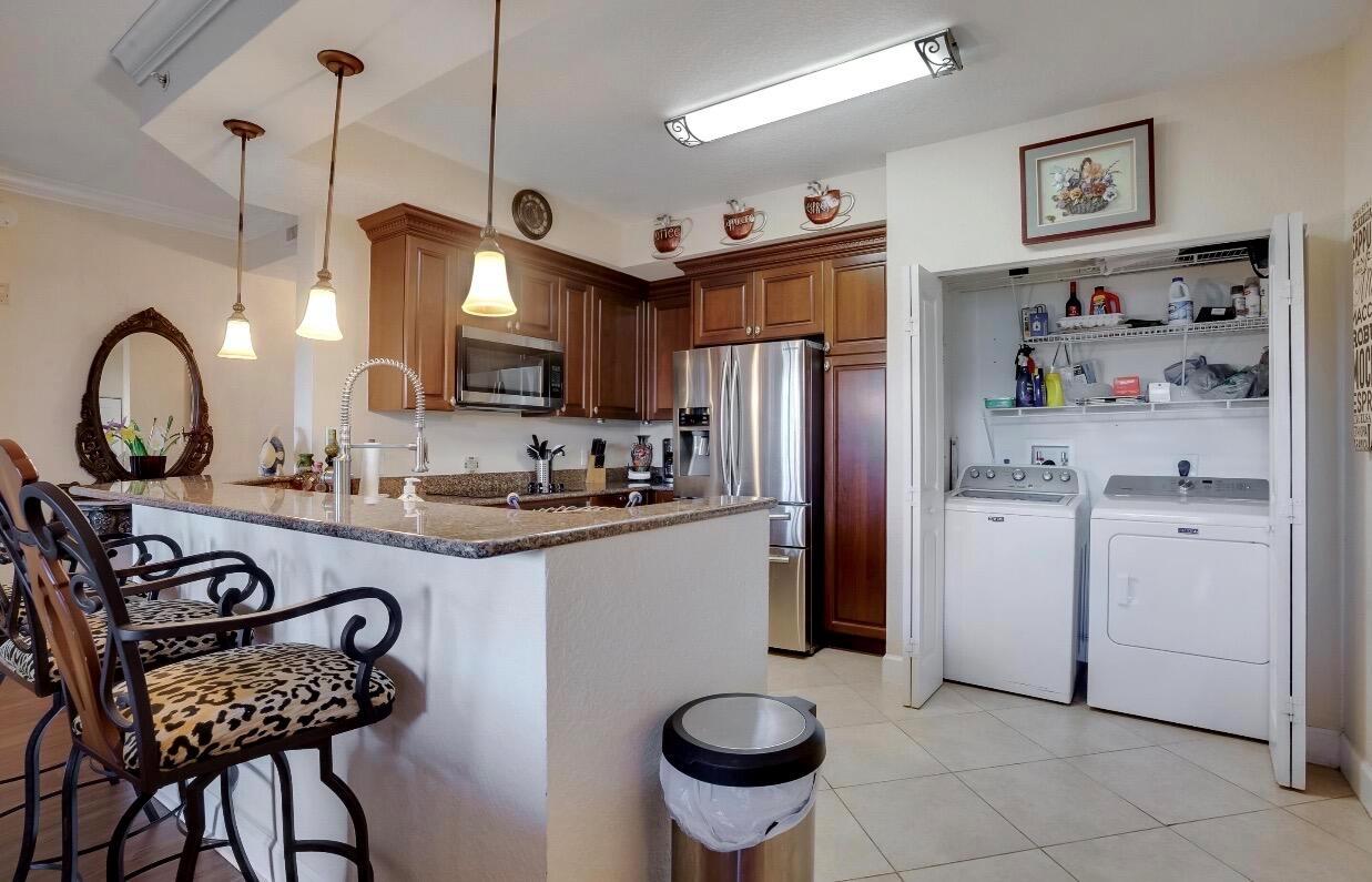 A kitchen with wood cabinets, granite countertops, stainless steel appliances, and an adjacent laundry closet — 1690 Renaissance Commons Boulevard # 1404, Boynton Beach FL 33426, BOYNTON BEACH, FL