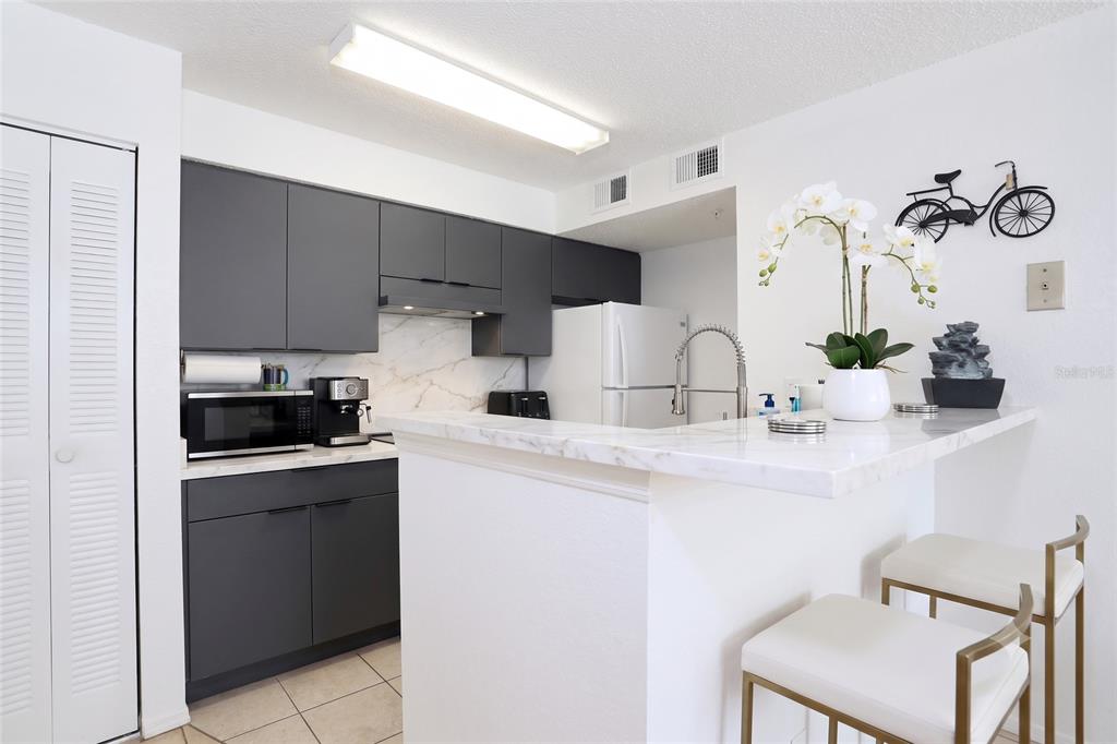 A kitchen features dark grey cabinets, white marble countertops, and a breakfast bar with stools — 2209 ANTIGUA PLACE UNIT 828, KISSIMMEE, FL