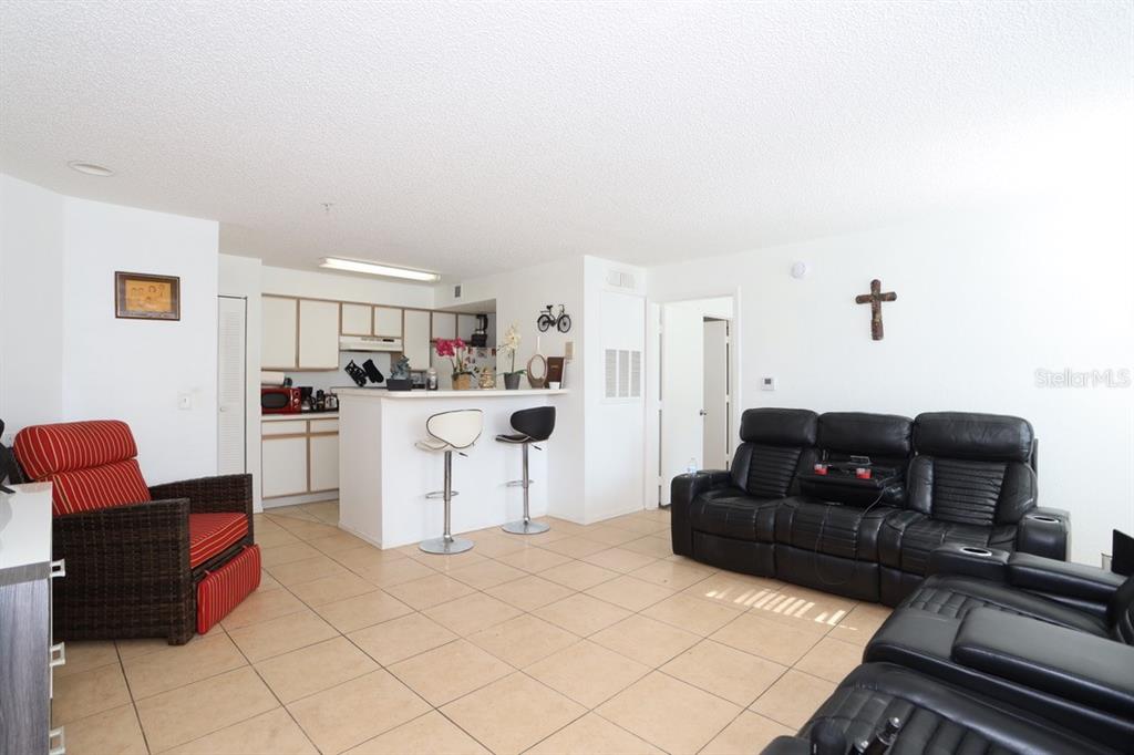 A living room with tile flooring, a kitchen breakfast bar, and black leather seating — 2209 ANTIGUA PLACE UNIT 828, KISSIMMEE, FL