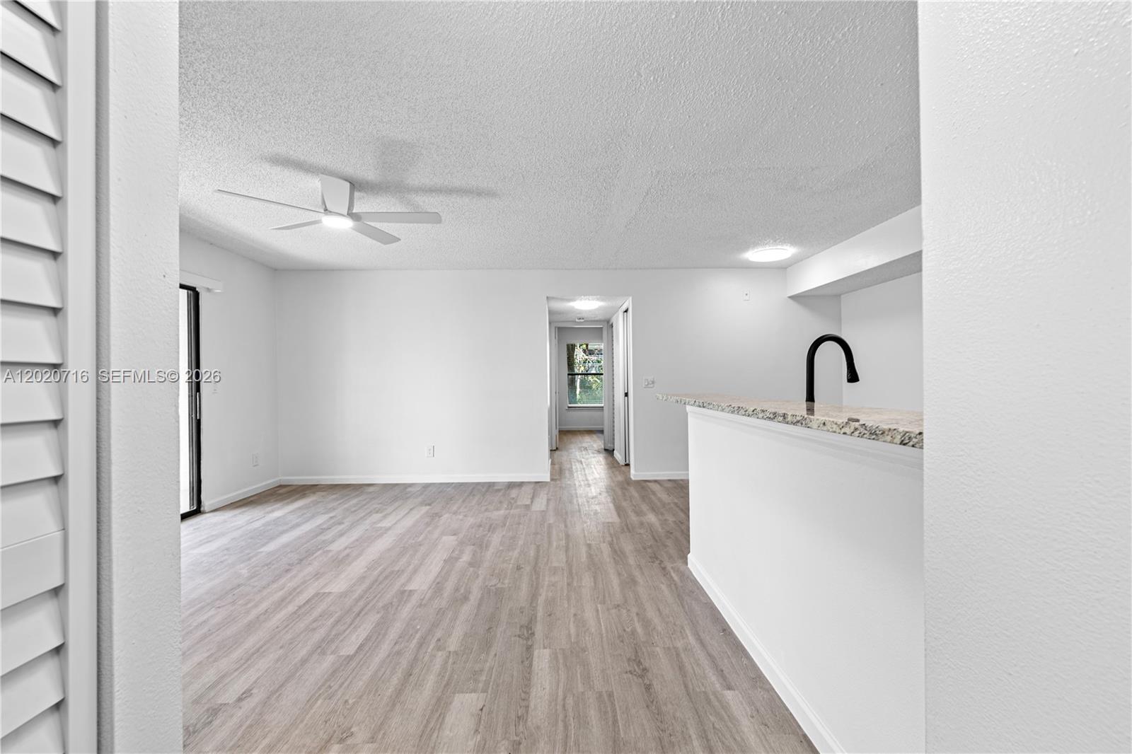 An open-concept living area features light wood-look flooring, a ceiling fan, and a kitchen counter — 2094 Arbour Walk Cir # 3018, Naples FL 34109, NAPLES, FL