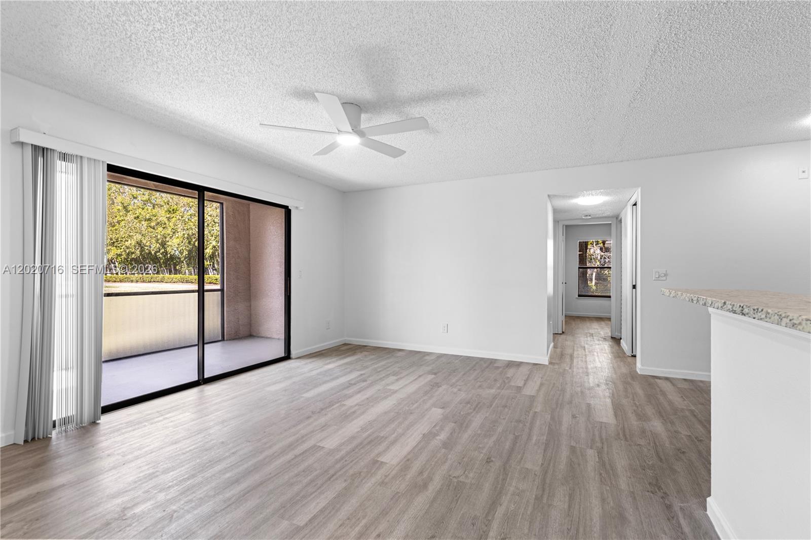 A living room with wood-look flooring, a ceiling fan, and sliding glass doors to a balcony — 2094 Arbour Walk Cir # 3018, Naples FL 34109, NAPLES, FL