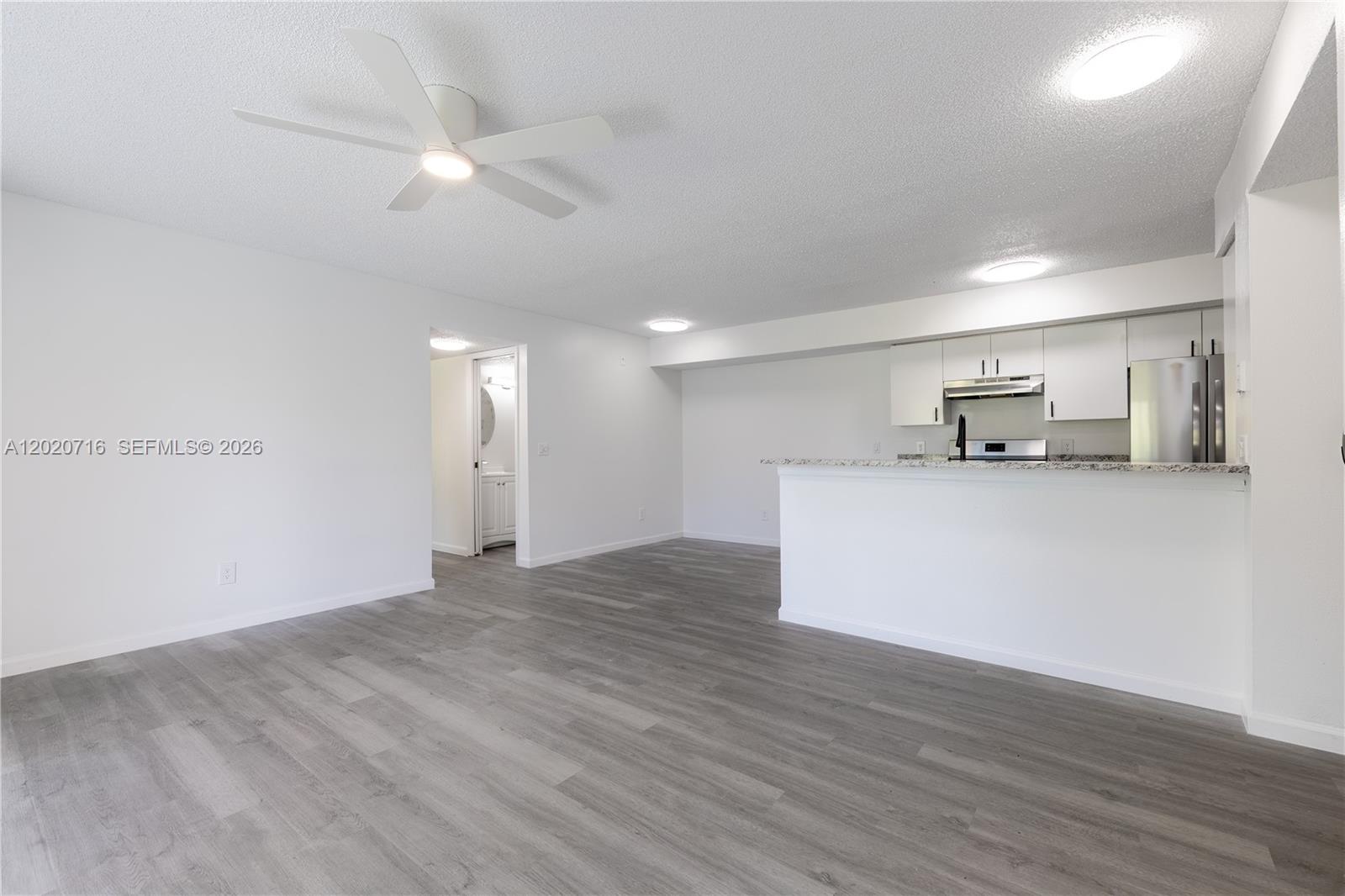 An open-concept living area features gray wood-look flooring, a white kitchen, and a ceiling fan — 2094 Arbour Walk Cir # 3018, Naples FL 34109, NAPLES, FL