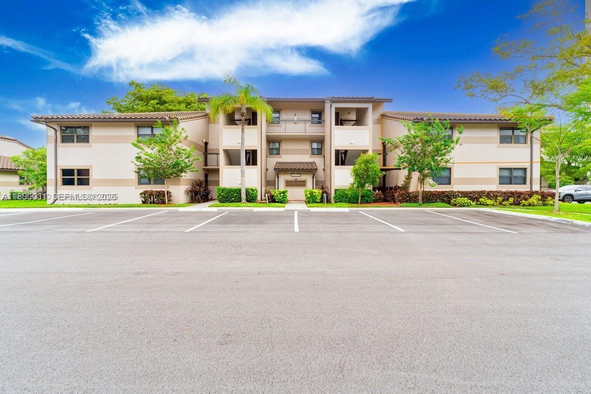 A three-story apartment building with a beige facade stands behind a paved parking lot — 9937 Nob Hill Pl # 1637, Sunrise FL 33351, SUNRISE, FL