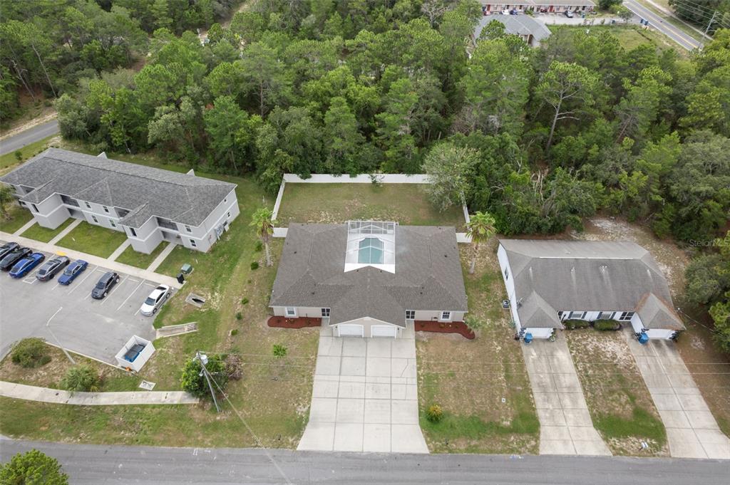 An aerial view shows three residential buildings, a parking lot, and a fenced backyard with a pool — 10370 SANDLOR STREET, SPRING HILL, FL