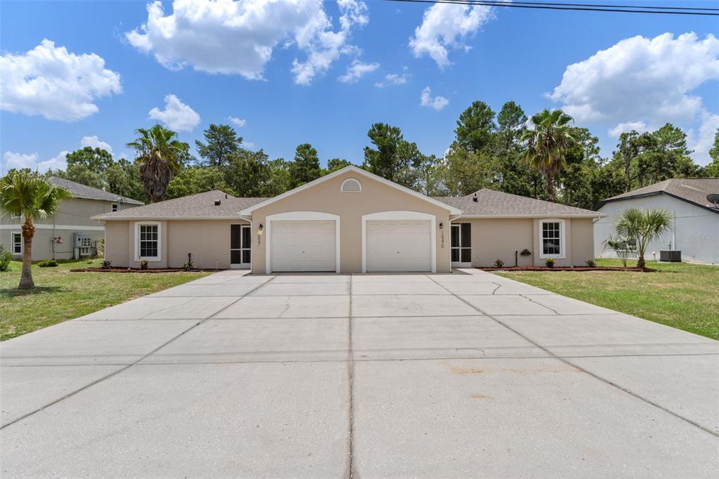 A duplex with two garage doors and a wide concrete driveway under a blue sky — 10370 SANDLOR STREET, SPRING HILL, FL