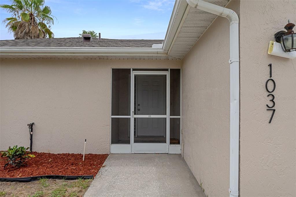 The exterior view shows a beige house entrance with a screen door and house numbers — 10370 SANDLOR STREET, SPRING HILL, FL