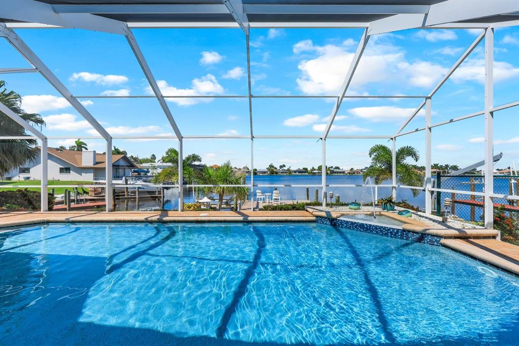 A swimming pool with a fountain sits inside a screened lanai overlooking a canal — 719 EL DORADO PARKWAY W, CAPE CORAL, FL