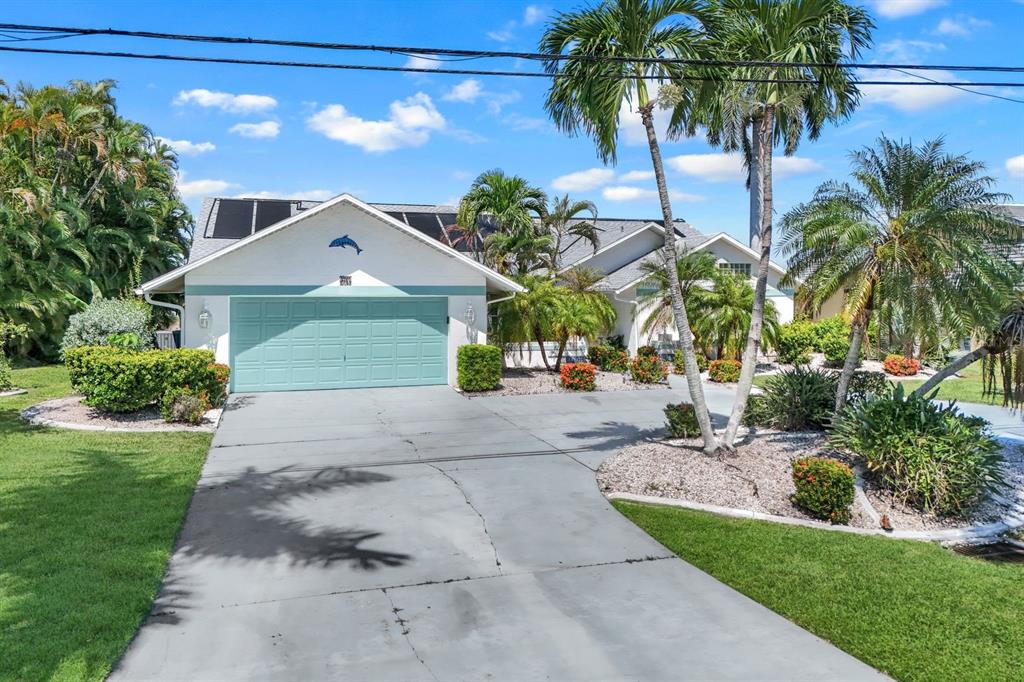 A single-story house with a teal garage door, solar panels, and palm trees in front — 719 EL DORADO PARKWAY W, CAPE CORAL, FL