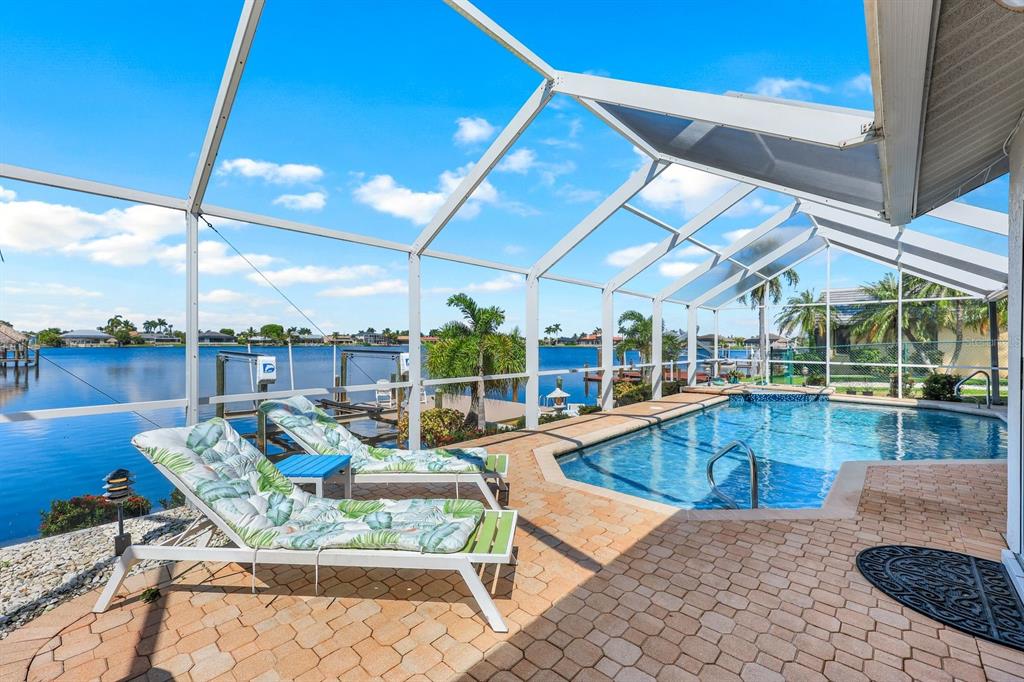 A screened-in pool patio features lounge chairs, brick pavers, and a view of the water — 719 EL DORADO PARKWAY W, CAPE CORAL, FL