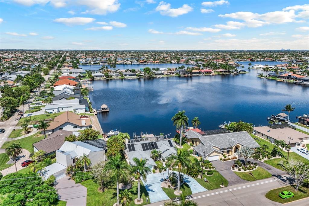 An aerial view shows waterfront homes with pools and docks along a large canal — 719 EL DORADO PARKWAY W, CAPE CORAL, FL