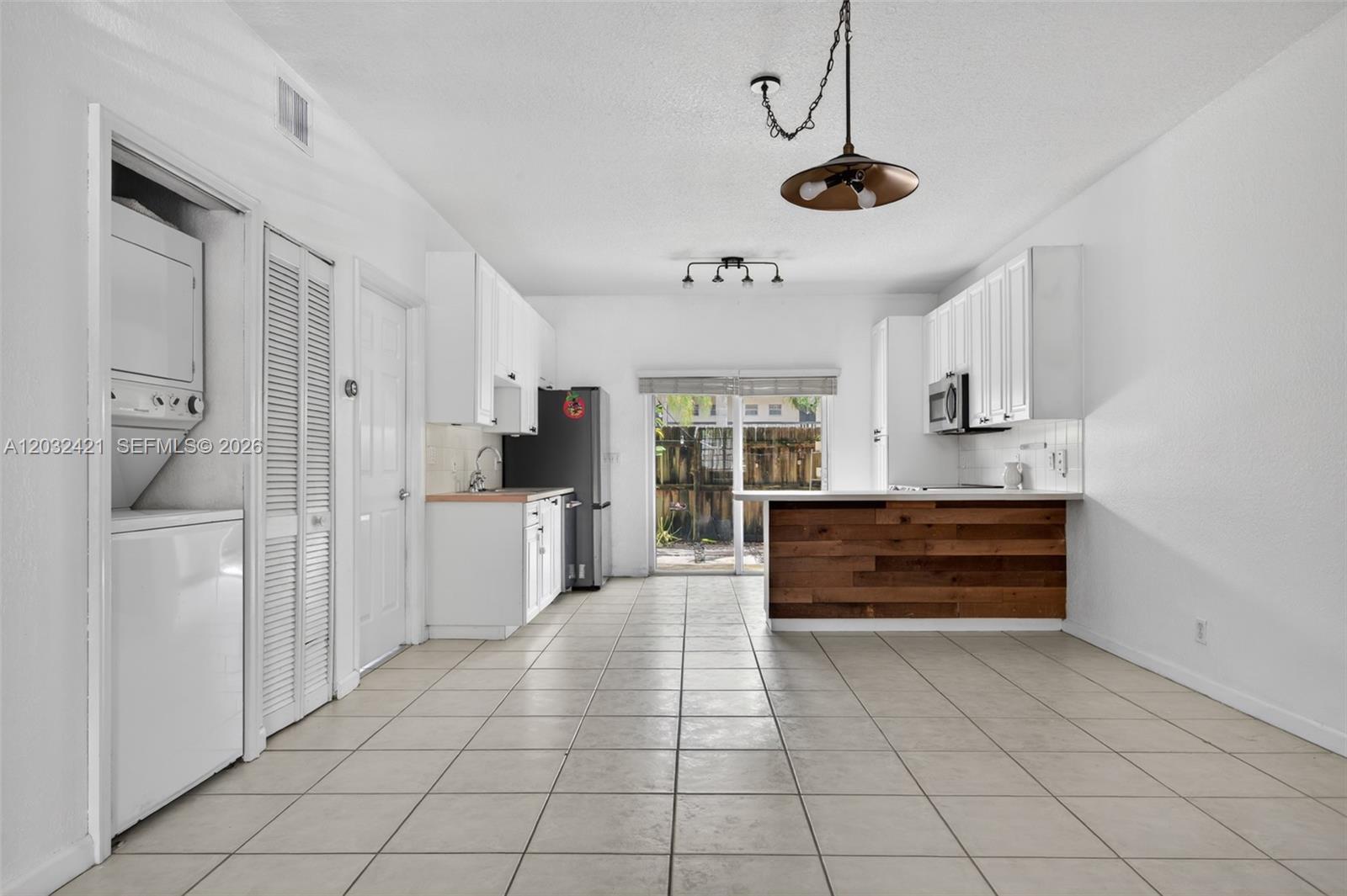 This kitchen features white cabinetry, a wood-paneled breakfast bar, tile flooring, and laundry appliances — 4902 Washington St # 4, Hollywood FL 33021, HOLLYWOOD, FL