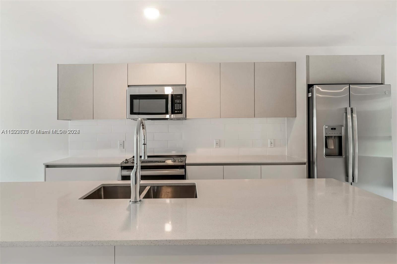 A modern kitchen features white cabinets, stainless steel appliances, and a large quartz-topped island — 2561 NE 193rd St # 1103, Miami FL 33180, MIAMI, FL