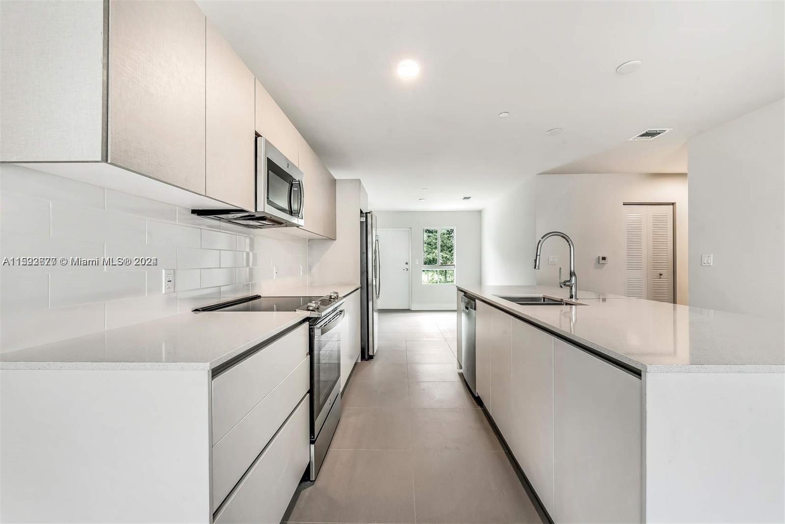 A modern kitchen features white flat-panel cabinetry, quartz countertops, stainless steel appliances, and tile flooring — 2561 NE 193rd St # 1103, Miami FL 33180, MIAMI, FL