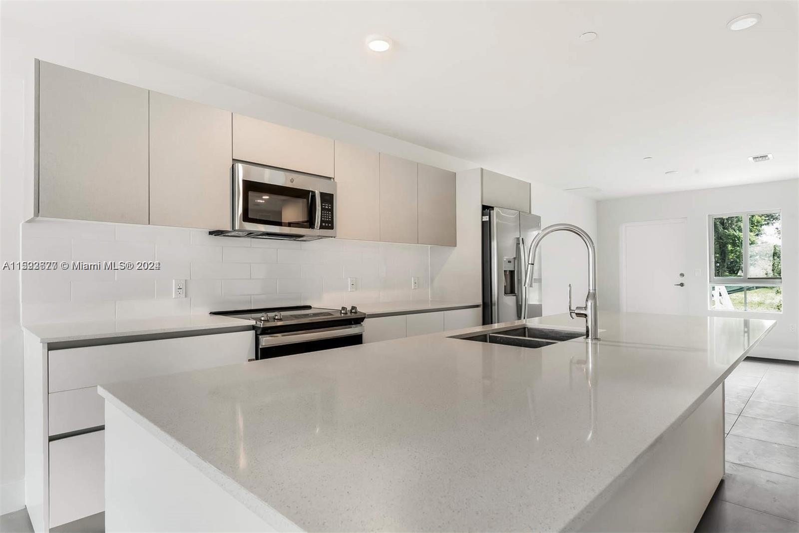 A modern kitchen features white cabinetry, a large quartz island, and stainless steel appliances — 2561 NE 193rd St # 1103, Miami FL 33180, MIAMI, FL