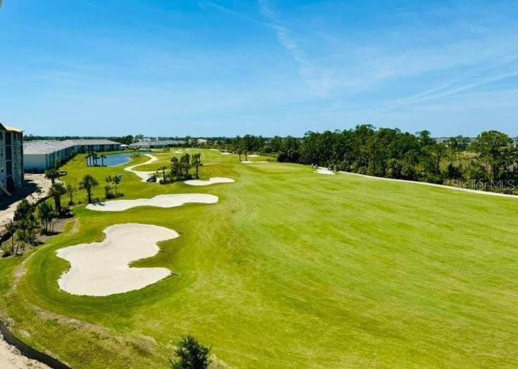 An aerial view shows a golf course fairway with sand bunkers and nearby residential buildings — 17445 OPAL SAND DRIVE UNIT 205, VENICE, FL