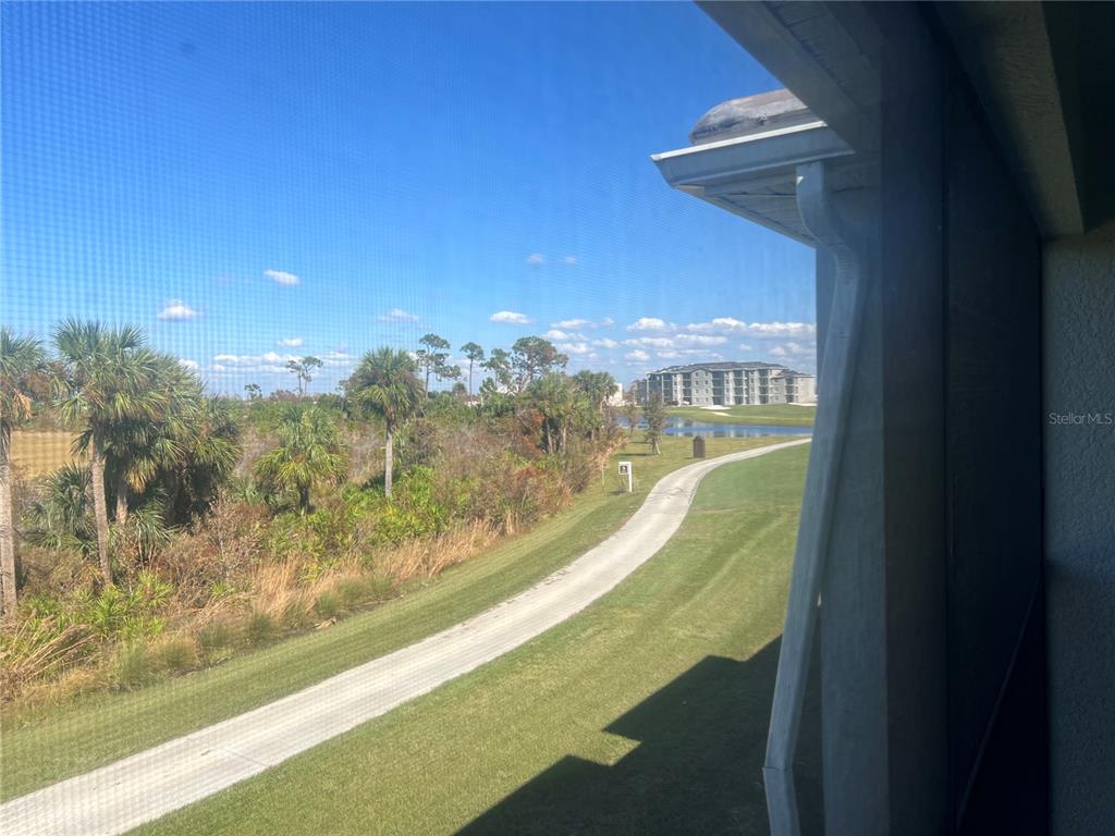 A view from a screened-in porch overlooking a grassy path, palm trees, and a pond — 17445 OPAL SAND DRIVE UNIT 205, VENICE, FL