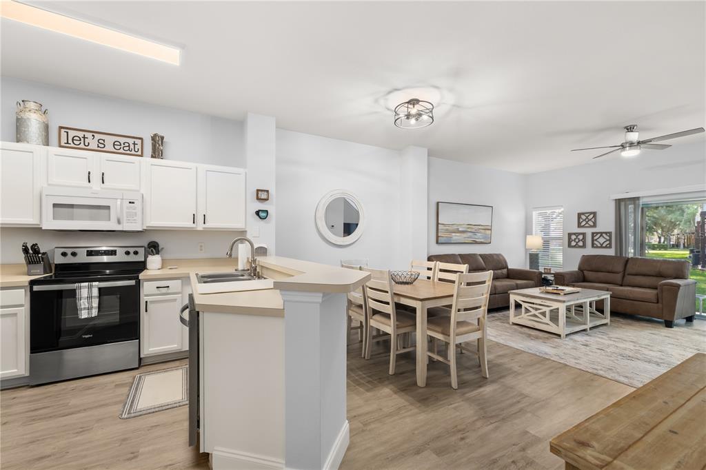 An open-concept kitchen, dining area, and living room feature light wood flooring and white cabinetry — 8424 CRYSTAL COVE LOOP, KISSIMMEE, FL