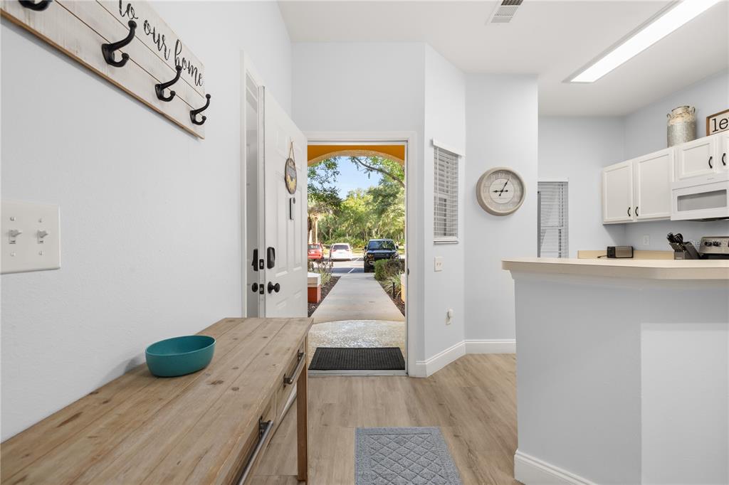 An entryway leads to an open kitchen with white cabinets and light wood flooring — 8424 CRYSTAL COVE LOOP, KISSIMMEE, FL