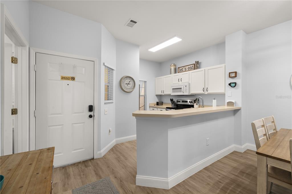A kitchen with white cabinets and a breakfast bar overlooks a dining area and entryway — 8424 CRYSTAL COVE LOOP, KISSIMMEE, FL