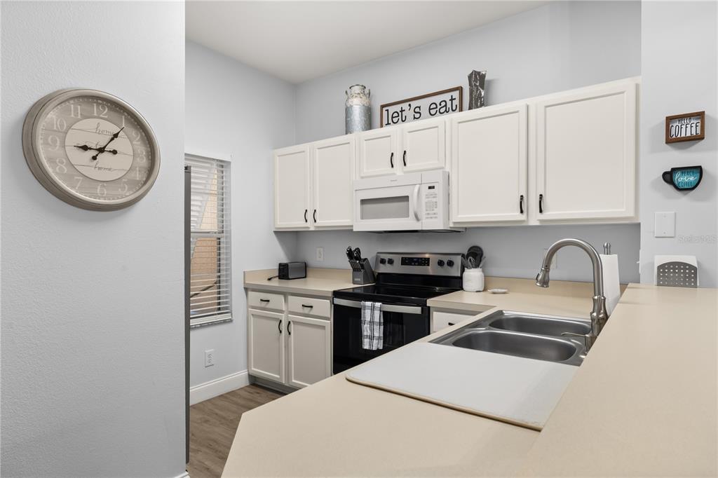 A kitchen features white cabinets, stainless steel appliances, and a beige countertop — 8424 CRYSTAL COVE LOOP, KISSIMMEE, FL