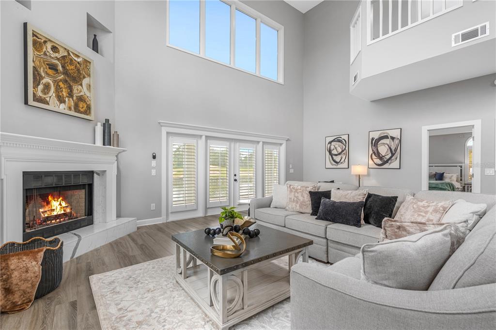A high-ceilinged living room features a fireplace, a large sectional sofa, and glass doors — 57 BAY POINTE DRIVE, ORMOND BEACH, FL