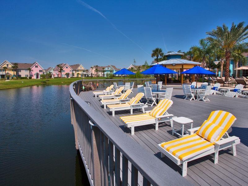 A wooden deck with lounge chairs and tables overlooks a pond near colorful residential houses — 5006 MANGROVE ALLEY UNIT 205, KISSIMMEE, FL
