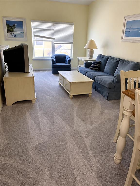 A living room features a blue sofa, a matching armchair, a coffee table, and carpeted floors — 5006 MANGROVE ALLEY UNIT 205, KISSIMMEE, FL