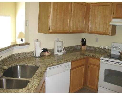 A kitchen with light wood cabinets, granite countertops, a double sink, and white appliances — 5006 MANGROVE ALLEY UNIT 205, KISSIMMEE, FL