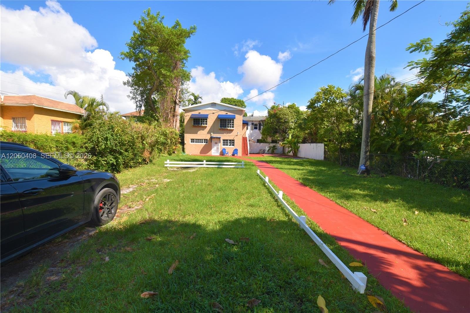 A two-story tan house features blue awnings, a red walkway, and a grassy front yard — 2615 SW 20th St, Miami FL 33145, MIAMI, FL