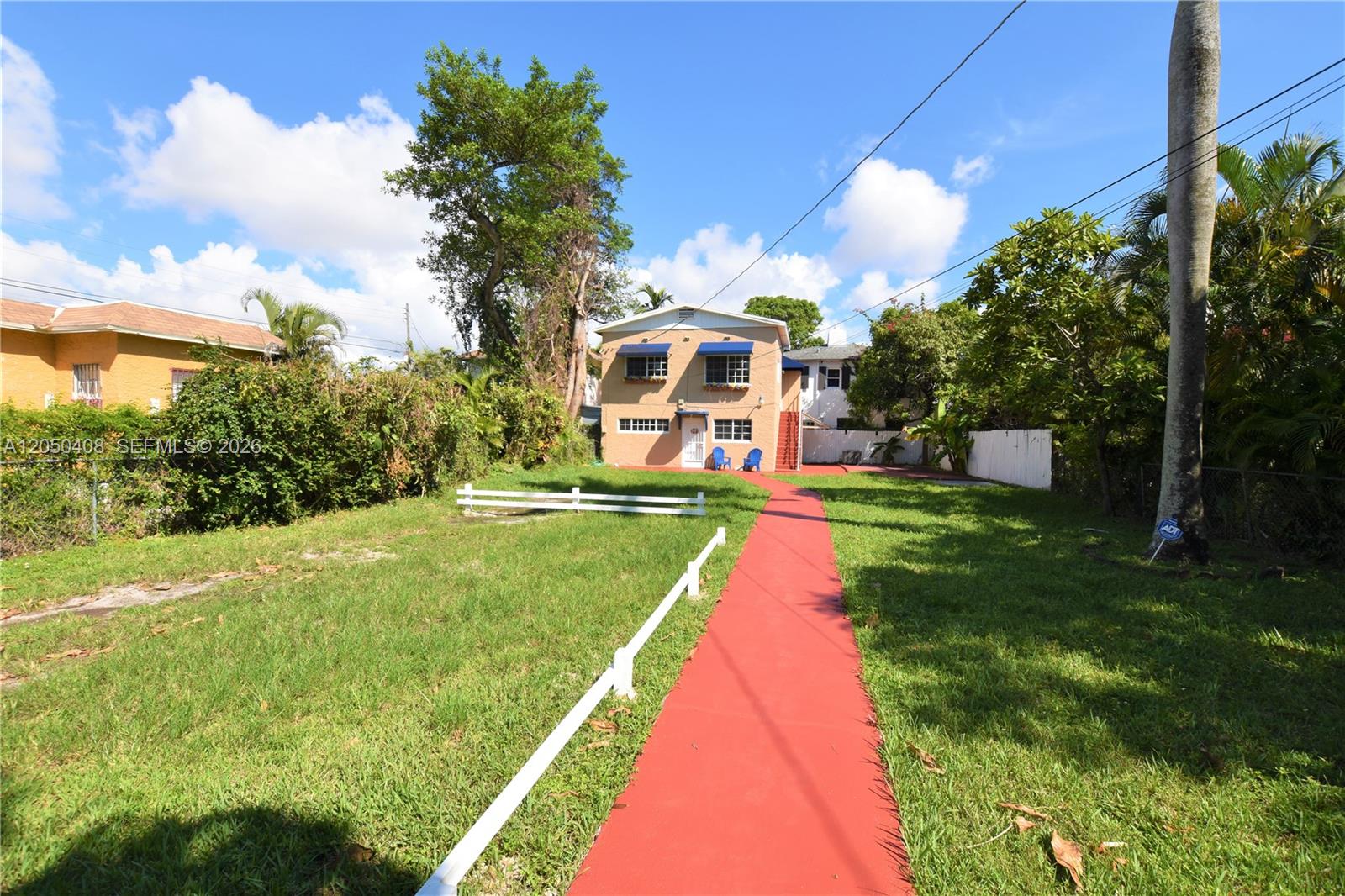 A red walkway leads to a two-story tan house with blue awnings and a lawn — 2615 SW 20th St, Miami FL 33145, MIAMI, FL