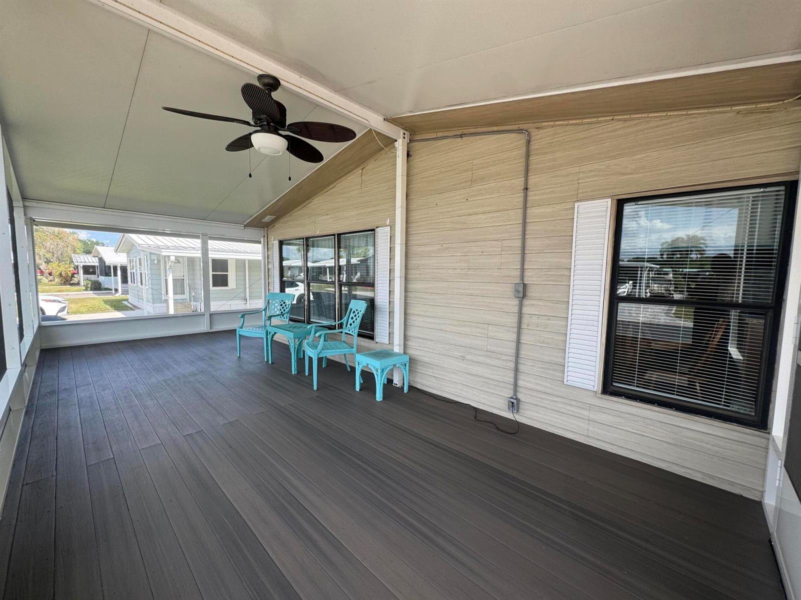 A covered porch features dark wood-look flooring, light siding, and two turquoise chairs — 1747 SW 35th Circle, Okeechobee FL 34974, OKEECHOBEE, FL