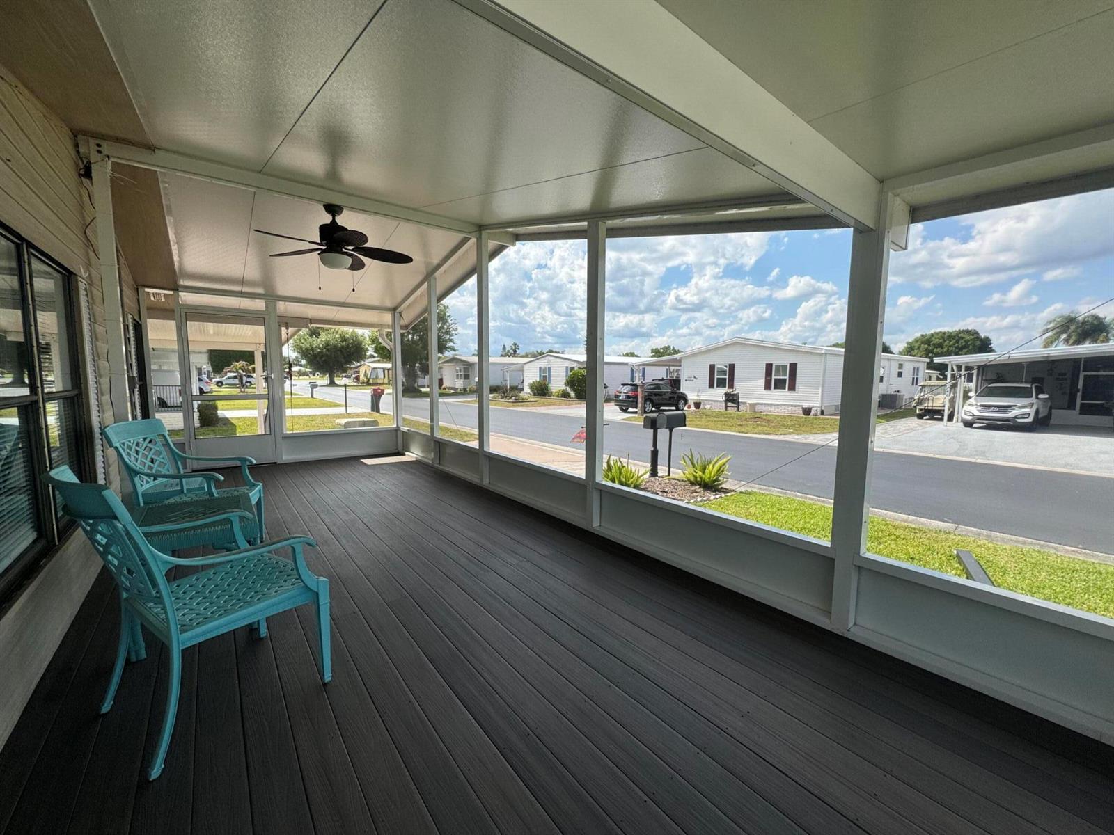 A screened-in porch features dark wood-look flooring, a ceiling fan, and two teal chairs — 1747 SW 35th Circle, Okeechobee FL 34974, OKEECHOBEE, FL