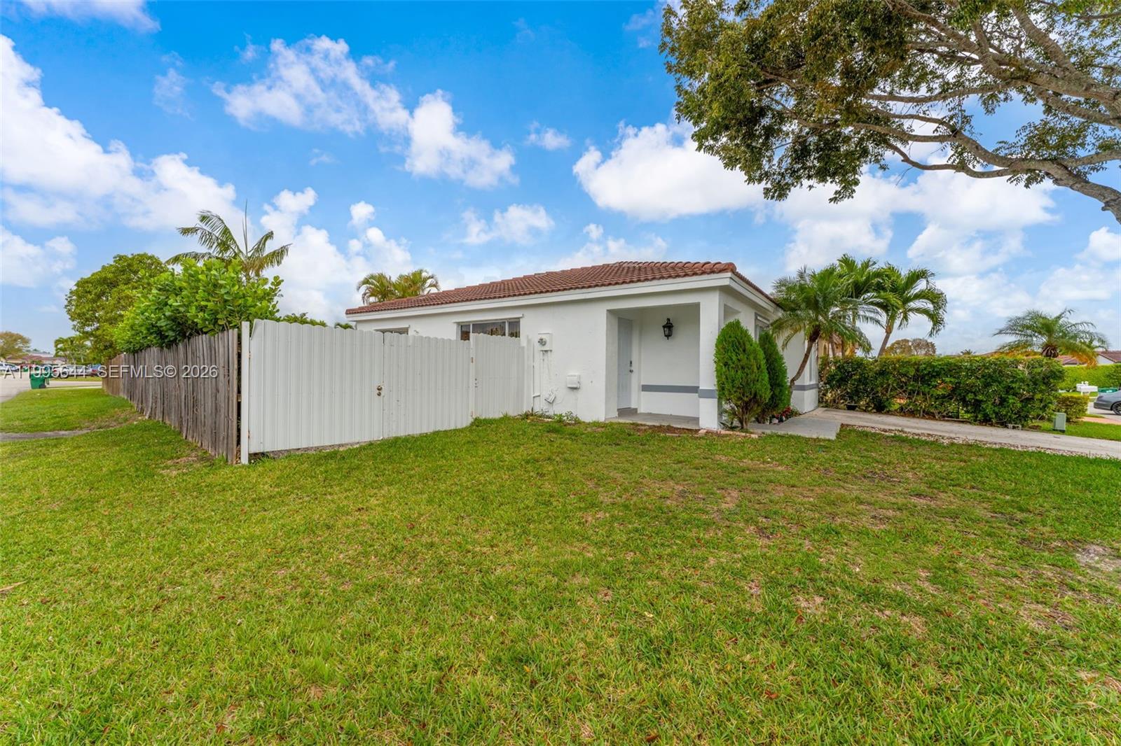 A white single-story house with a tile roof stands behind a white privacy fence — 17570 SW 142nd Ct, Miami FL 33177, MIAMI, FL