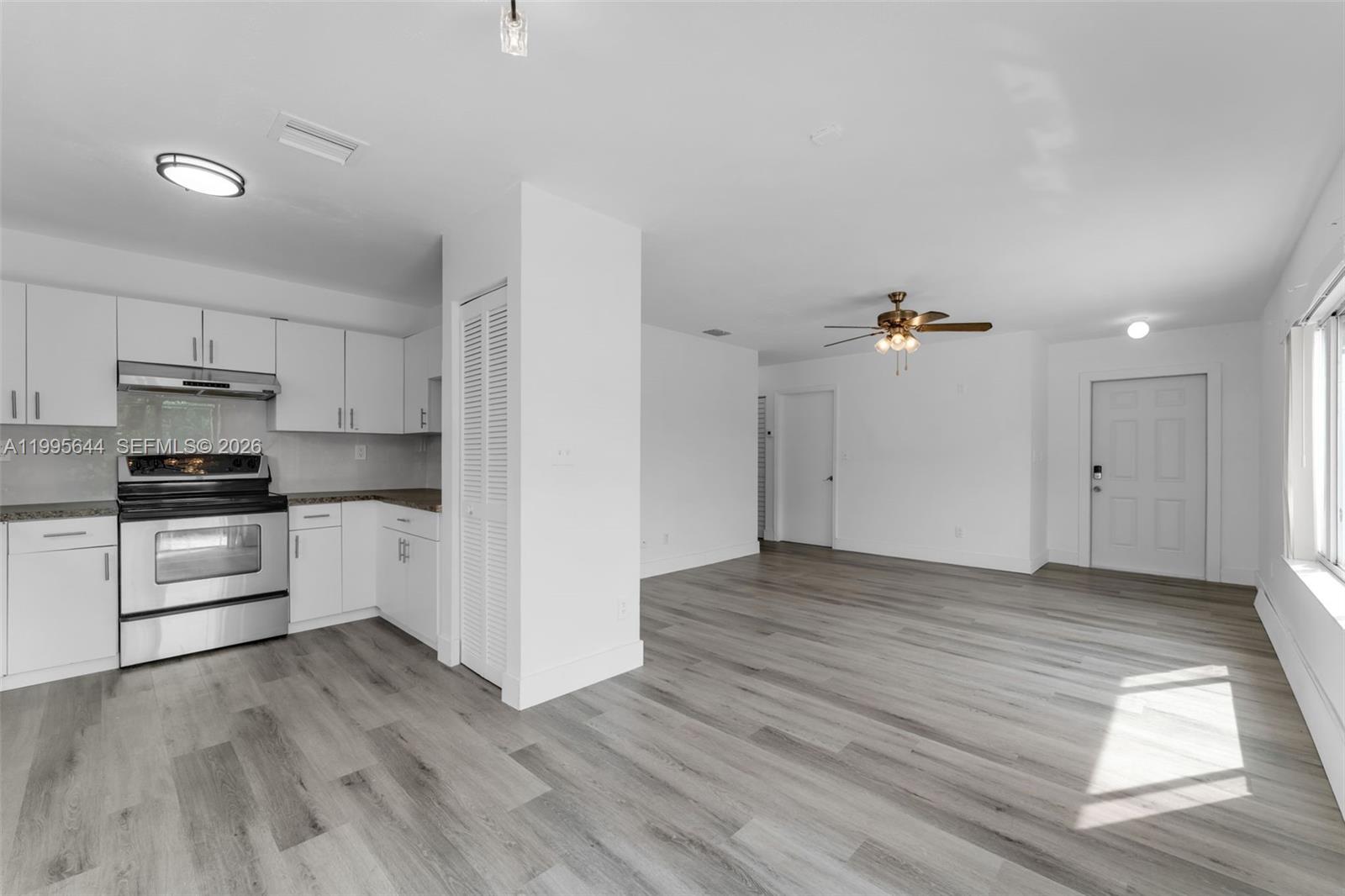 A kitchen with white cabinets and stainless steel appliances opens into a living area — 17570 SW 142nd Ct, Miami FL 33177, MIAMI, FL