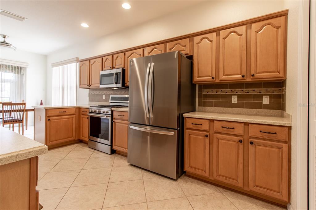 A kitchen features light wood cabinets, stainless steel appliances, and a tiled backsplash — 16205 SW 12TH TERRACE, OCALA, FL