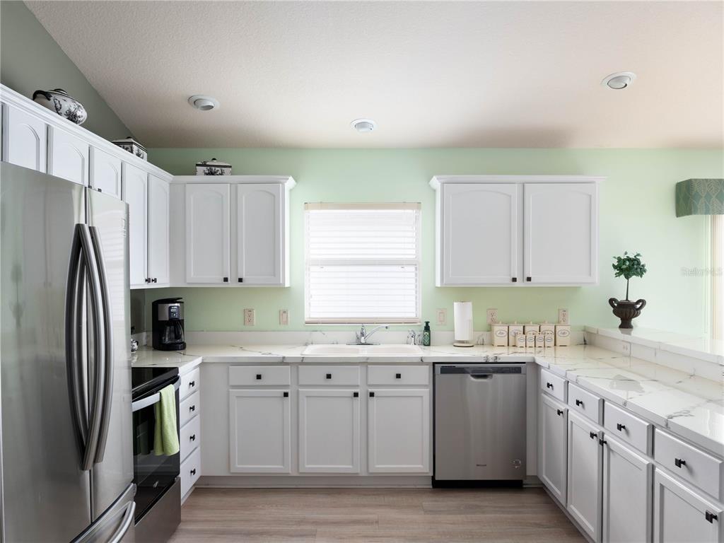 A kitchen features white cabinets, stainless steel appliances, and light-colored countertops against pale green walls — 2453 VIOLET COURT, THE VILLAGES, FL