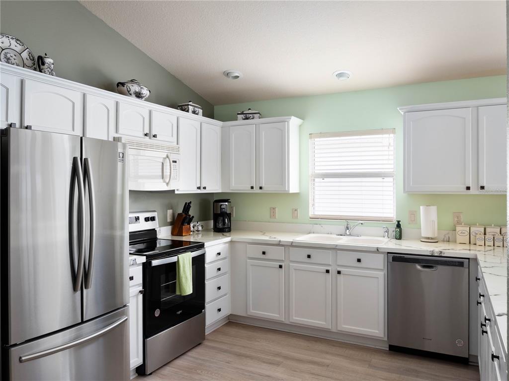 A kitchen features white cabinets, stainless steel appliances, light countertops, and pale green walls — 2453 VIOLET COURT, THE VILLAGES, FL