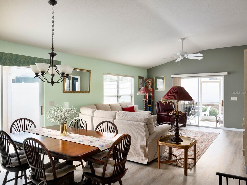 An open-concept living and dining area features light green walls, wood-look flooring, and sliding doors — 2453 VIOLET COURT, THE VILLAGES, FL