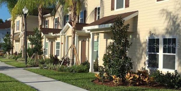 The exterior of a multi-story tan townhouse building features a sidewalk and landscaped front yard — 3225 CUPID PLACE, KISSIMMEE, FL