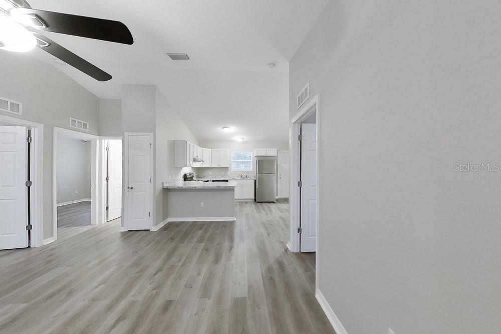 A living area with wood-look flooring leads to an open kitchen with white cabinets — 6771 SW 149TH LANE ROAD, OCALA, FL