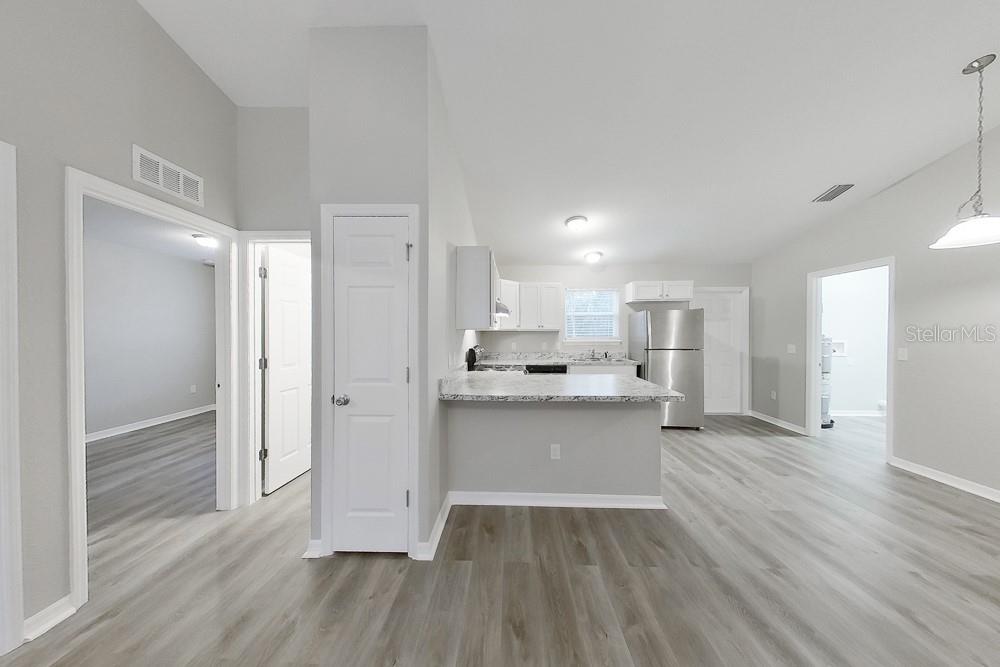 A kitchen with white cabinets and stainless steel appliances overlooks a living area with flooring — 6771 SW 149TH LANE ROAD, OCALA, FL